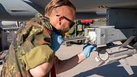 Ein Soldat drückt mittels eines Metallrohrs mit einem Plastikaufsatz von hinten fest gegen den Dispenser des Eurofighters.