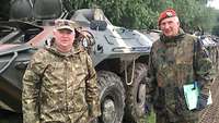 Zwei Stabsoffiziere stehen in grüner Uniform im Gelände vor einem rumänischen Schützenpanzer.