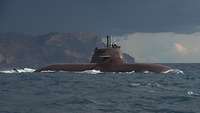 A dark grey submarine off a coast.