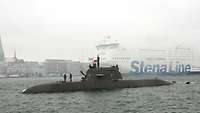 A dark grey submarine in a fjord.