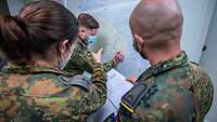 Mehrere Soldatinnen und Soldaten stehen vor einer Karte.