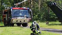 Ein Feuerwehrfahrzeug löscht mit dem Strahlrohr auf dem Dach, davor kniet ein Feuerwehrmann.