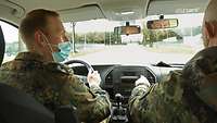 Zwei Soldaten sitzen in einem PKW, vor ihnen ein Parcours auf der Straße