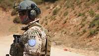 Soldat mit Schutzausrüstung und Waffe steht auf unbefestigtem Weg