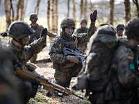Meine Innere Führung Mehrere Soldaten hocken im Wald zusammen. Eine Soldat in der Mitte hebt dabei die Hand.