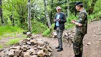 Auf einem Trampelpfad in einem Wald unterhält sich ein General mit einem Zivilisten.