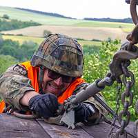 Ein Soldat verzurrt bei der Bahnverladung eine Kette. Er trägt einen Gefechtshelm und eine orangfarbene Warnweste.