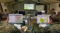 Zwei Soldaten sitzen vor ihren Computern. Auf den Bildschirmen sind Karten zu sehen.