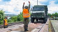 Ein Soldat steht auf einem Bahnwaggon. Er trägt eine leuchtende Warnweste und hält beide Arme nach oben.