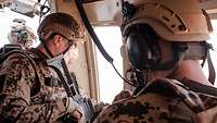 Zwei Soldaten sitzen an der geöffneten Tür eines fliegenden Hubschraubers