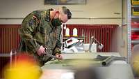 Ein Soldat schneidet in ein Stück Stoff, das vor ihm auf einem Tisch ausgebreitet liegt.