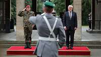 Bundespräsident Steinmeier und ein salutierender Soldat stehen nebeneinander auf einem roten Podest