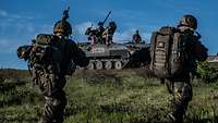 Deutsche Soldaten in Gefechtsanzug rennen am Boden, im Hintergrund steht ein rumänischer Schützenpanzer.