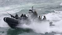 Navy personnel in battle dress on a moving rigid-hulled inflatable boat.