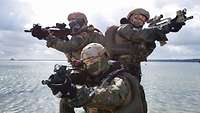 Three service members in battle dress carrying assault rifles pose for the photographer.