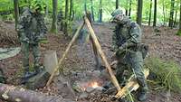 Zwei Soldaten stehen neben eine Holzfeuer, das bereits brennt.