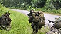 Seitlich an einem Waldweg im hohen Gras sind Soldaten mit ihren Waffen im Anschlag.