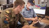 Zwei Marineoffiziere Sitzen vor einem Touchscreen und werten die aus der Luft stammenden Informationen aus.