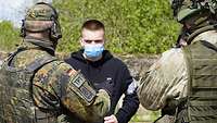 Zwei Soldaten stehen vor einem zivil gekleideten Übungsteilnehmer und unterhalten sich mit ihm
