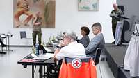 Eine Jacke vom Deutschen Roten Kreuz im Vordergrund auf einer Stuhllehne; auf dem Stuhl sitzt Rüdiger Unger