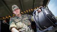 Soldat hält eine Kabeltrommel in der Hand.