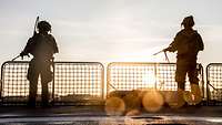 Two service members standing on a flight deck at sunset.