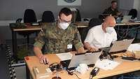 Ein Soldat und ein Ziviler Mitarbeiter sitzen nebeneinander an einem Tisch.