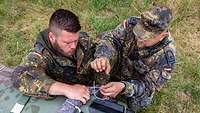 Zwei Soldaten stehen vor einem Geländewagen und umwickeln Lastgurte mit einem Vlies.