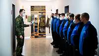 Rekrutinnen und Rekruten stehen auf einem Flur und ein Soldat erklärt ihnen den Spindbau. 