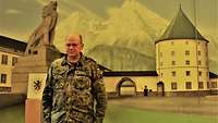 Ein Soldat steht vor einem Wandgemälde mit Bergen und Gebäuden.