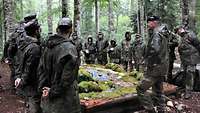 Zahlreiche Soldaten stehen im Wald um ein Geländemodell herum.
