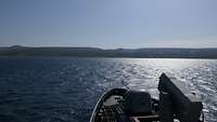 Im Hintergrund liegt eine Berglandschaft. Im Vordergrund fährt ein Boot im Meer