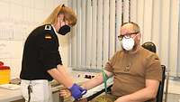 Ein Soldat sitzt im Behandlungszimmer, eine Sanitätssoldaten bereitet am Arm einen Zugang vor.