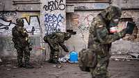 Soldaten in ABC-Schutzkleidung mit Arbeitsgeräten vor einer mit Graffiti besprühten Wand in einer Industruieruine