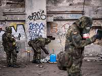 Soldaten in ABC-Schutzkleidung mit Arbeitsgeräten vor einer mit Graffiti besprühten Wand in einer Industruieruine
