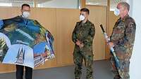 Ein Mann im Anzug überreicht zwei Soldaten einen Regenschirm mit Bildern der Stadt.