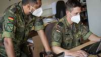 Zwei Soldaten mit Mund-Nasenschutz arbeiten gemeinsam an ihren Laptops.