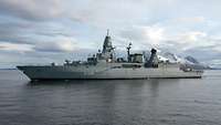 A grey ship is underway on a body of water.