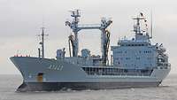 A grey ship is underway on a body of water.