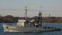 A grey ship is underway on a body of water.
