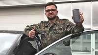 Ein Soldat steht in einer Autotür und hält ein Handy hoch.
