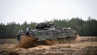 Ein deutscher Panzer fährt auf einer unwegsamen Sandfläche. Ein Soldat schaut aus der Luke