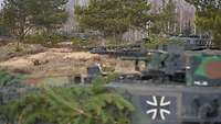 Mehrere Kampfpanzer der deutschen Kräfte stehen am Waldrand. Alle zielen in die gleiche Richtung