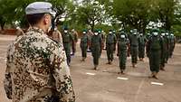 Im Vordergrund ein deutscher Soldat Im Hintergrund mehrere angetretene malische Soldaten