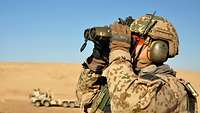 Ein Soldat mit Helm schaut durch ein Doppelfernrohr in der Wüste