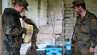 Eine Soldatin und ein Soldat bauen an einem Tisch Laborgeräte auf. Im Hintergrund steht ein weiterer Soldat