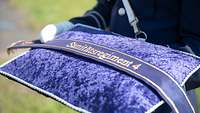 Auf einem violetten Samtkissen liegt ein schmales, ebenfalls violettes Band mit dem Schriftzug Sanitätsregiment 4 darauf