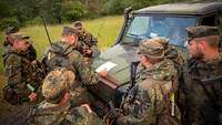 IT-Soldaten stehen an einem militärisches Fahrzeug und halten eine Lagebesprechung ab.