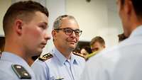 Ein General in blauem Hemd des Dienstanzuges steht inmitten einer Gruppe Soldaten und spricht mit ihnen.