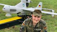 Ein junger Soldat lächelt in die Kamera, im Hintergrund steht eine Drohne am Boden.